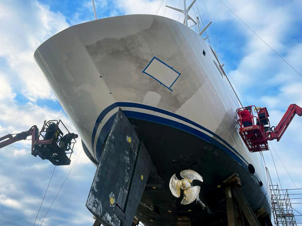 Diesel soot staining on a large yacht hull. Shipyard workers on boom lifts working on the hull. 